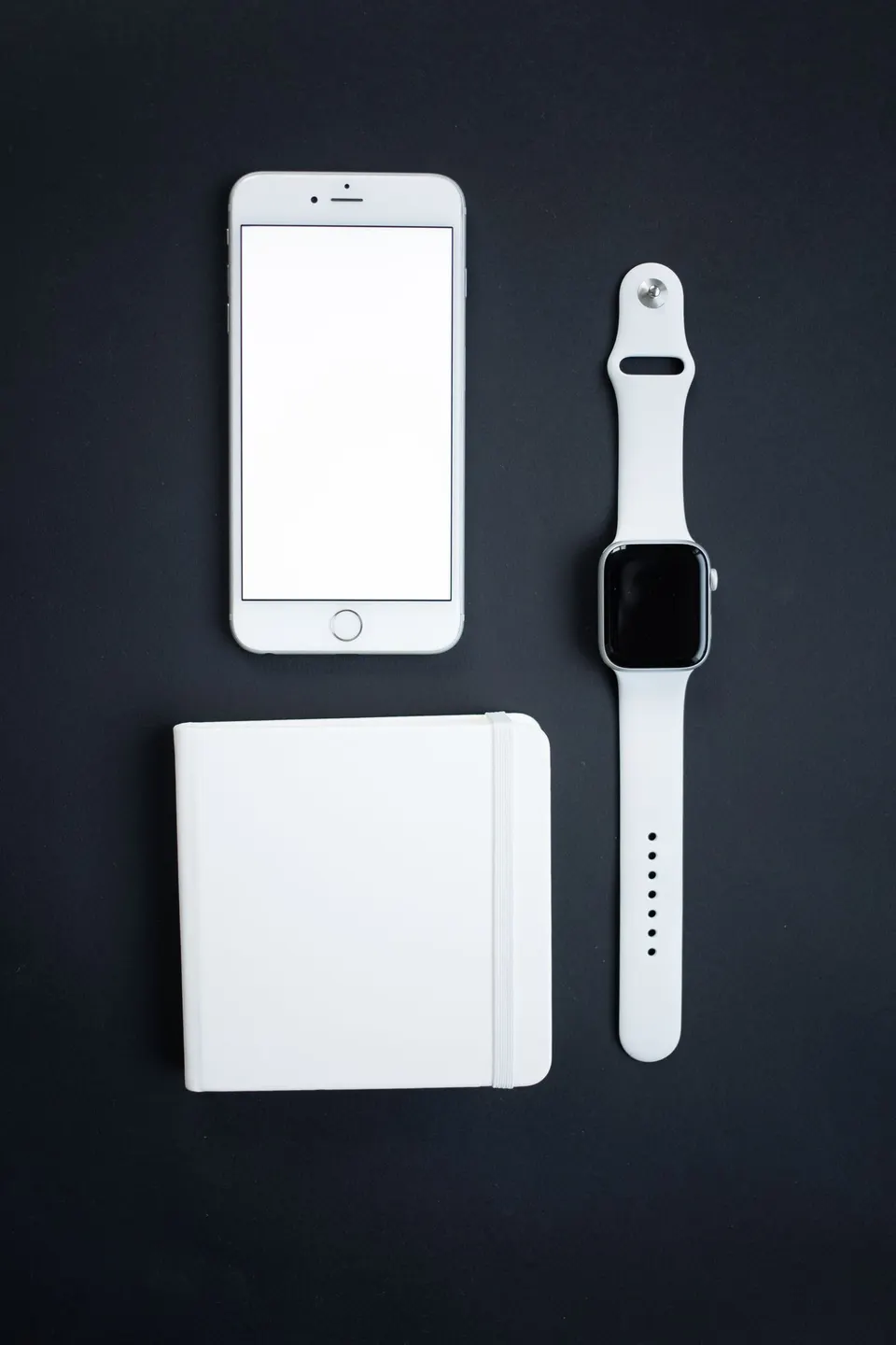 A smartphone, smartwatch and notebook arranged on a dark surface.