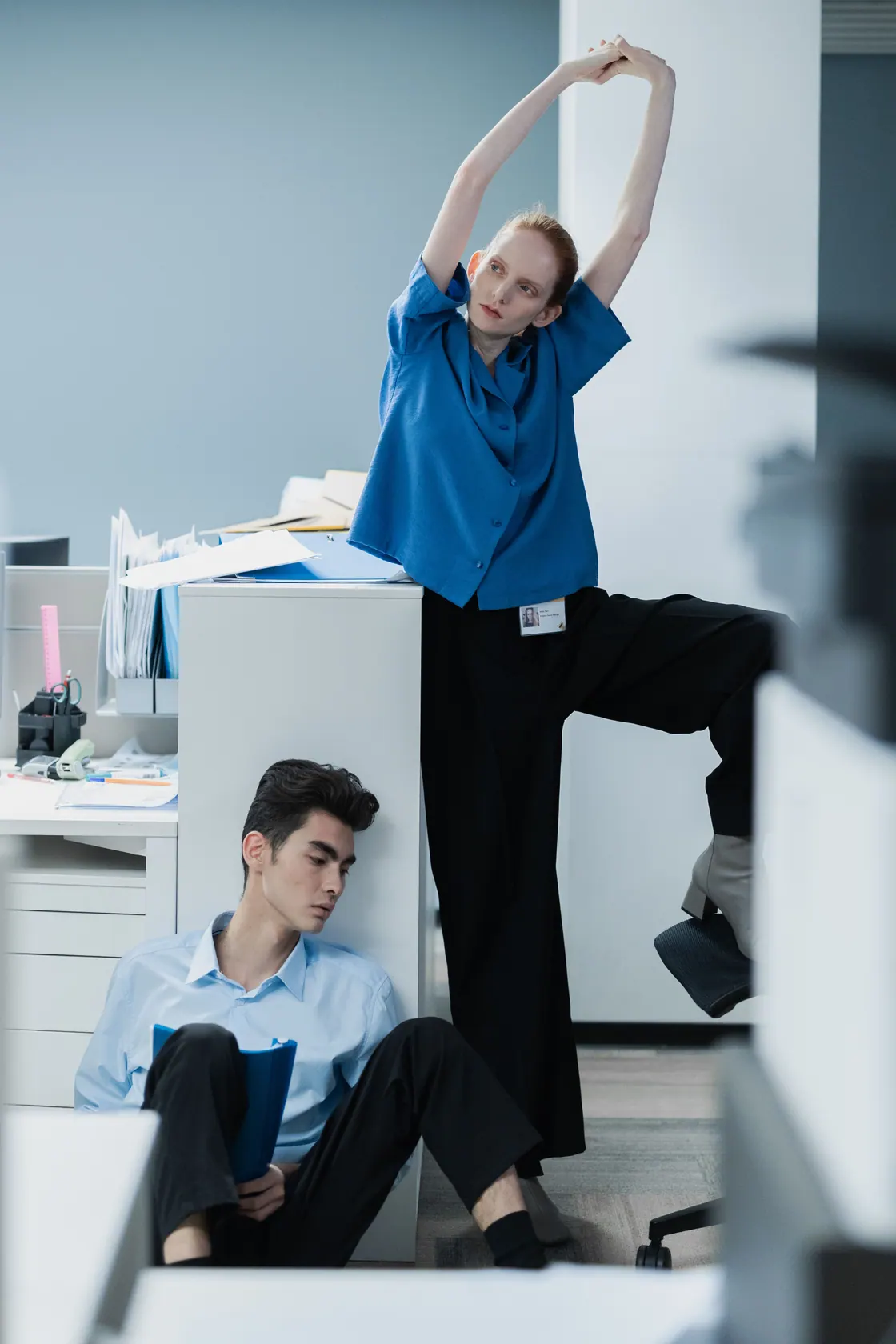 Two office workers taking a stretching break beside a desk.