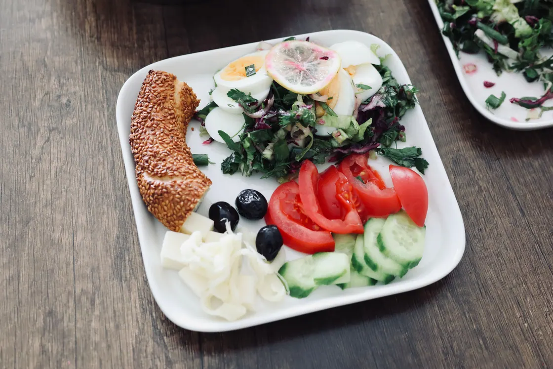 A breakfast plate with eggs, cucumber, tomato, olives, cheese and bread.