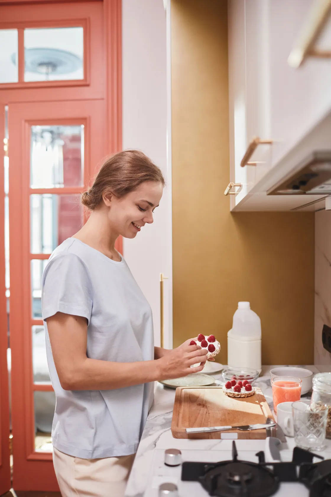 A woman preparing breakfast with berries and a bottle of milk on a kitchen counter.