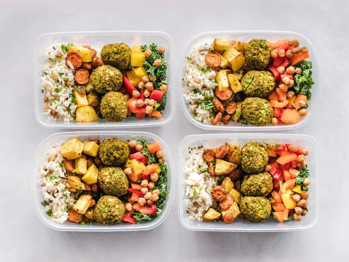 Four meal containers filled with rice, vegetables, chickpeas and falafel.