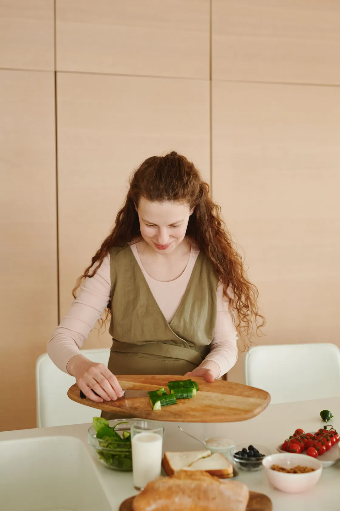 A woman sliding chopped green pepper from a wooden board into a glass bowl.