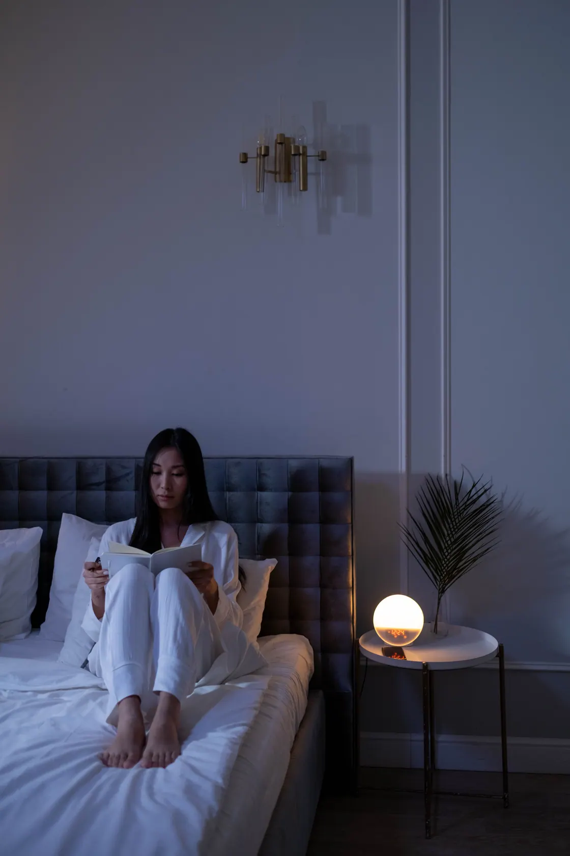 A woman reading in bed beside a softly glowing bedside lamp.