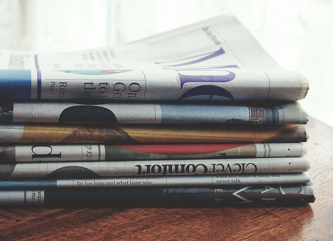 A stack of folded newspapers on a wooden table.