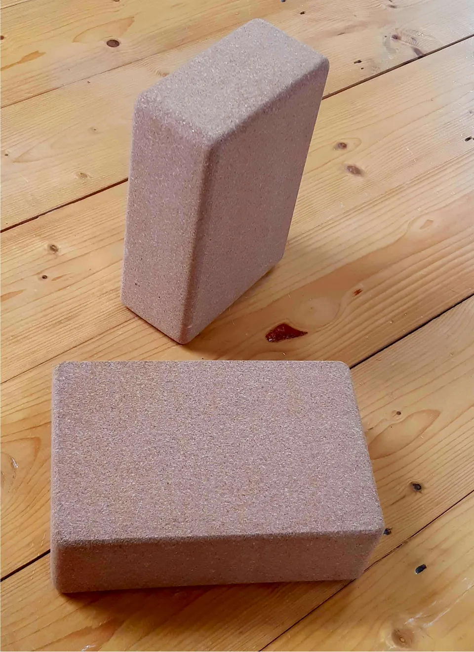 Two rectangular cork yoga blocks, one upright and one lying flat, on a wooden floor.