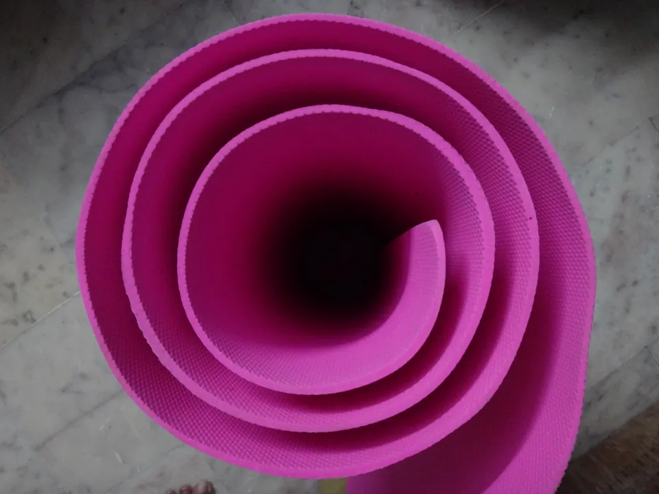 A bright pink yoga mat rolled into a spiral, viewed from above.