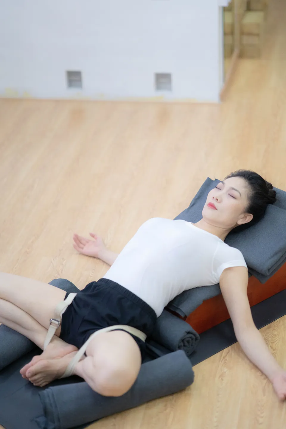 A woman reclining on stacked supports with knees bent outward and cushions supporting the legs.