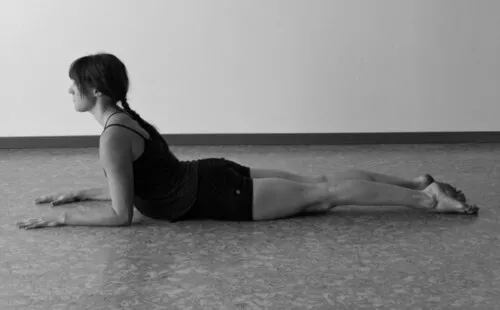 A person lying face down with the chest raised and forearms resting on the floor, in a black-and-white photograph.